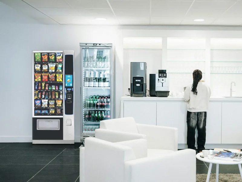 Snack vending machine beside a drinks cooler in a bright office break room